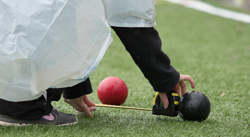 Arbitre accroupi mesurant la distance entre deux balles de boccia sur un terrain en gazon.