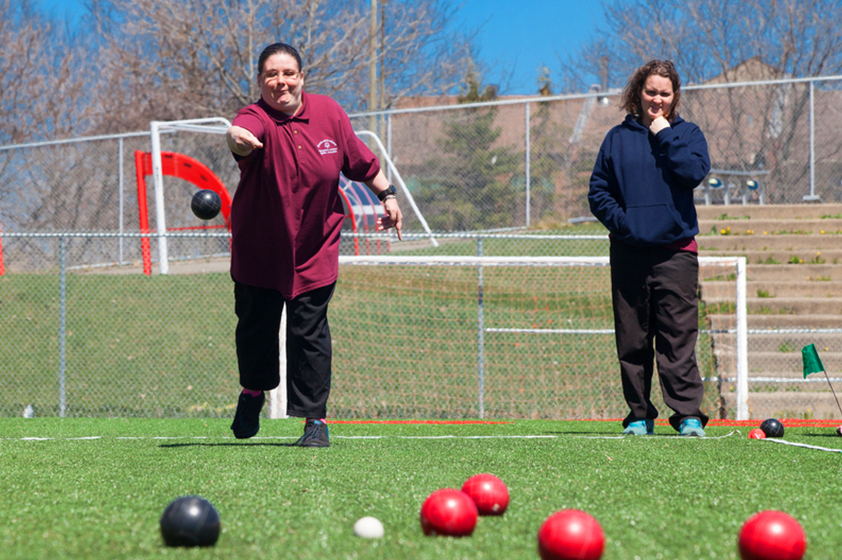 An athlete throwing a boccia ball on a natural turf pitch.