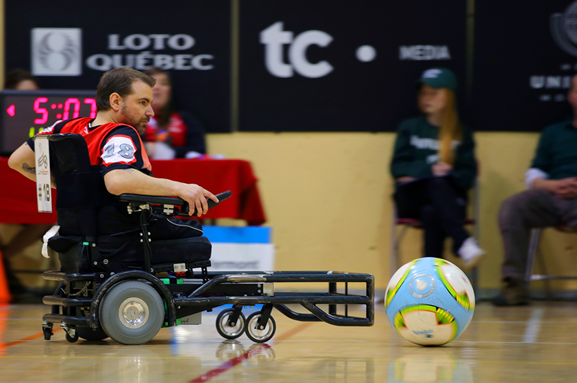 Un athlète en fauteuil roulant en action pendant un match de powerchair soccer. 