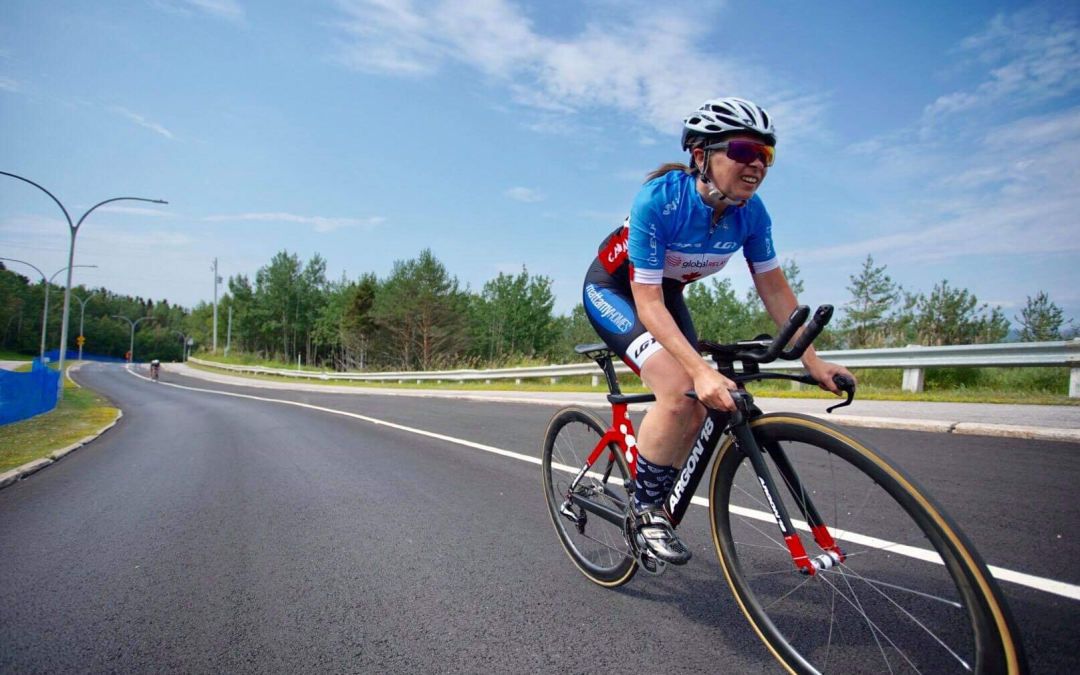 Description de l'image : Marie-Claude Molnar pédale à vélo sur une route en se dirigeant vers la droite de la caméra.