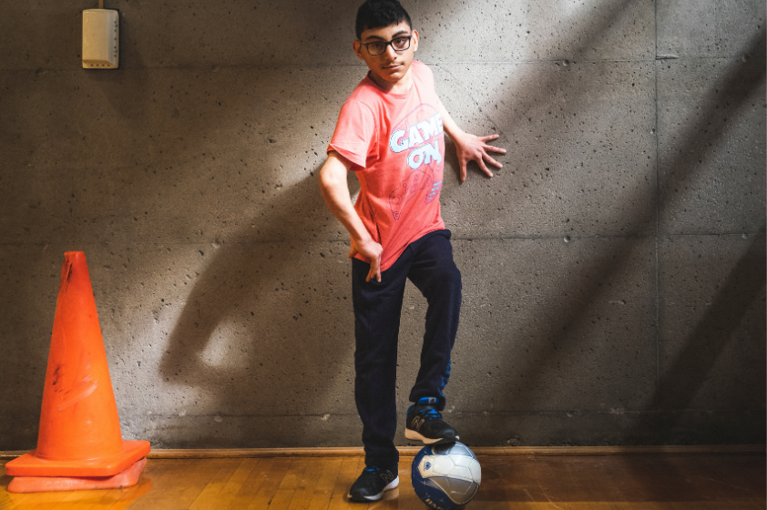 Un garçon prend la pause devant un mur de béton en posant un pied sur ballon de soccer.