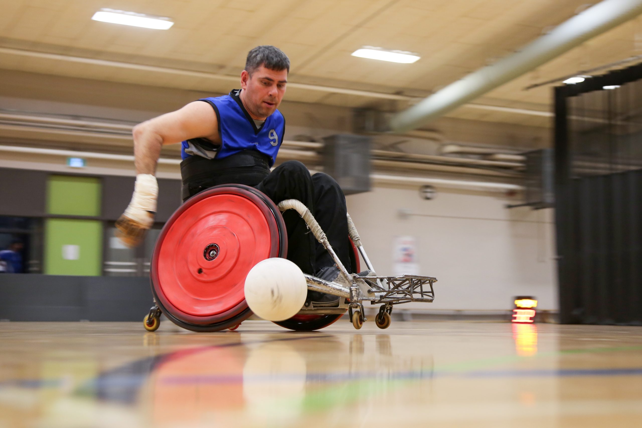 Description de l'image : Au centre, un athlète de rugby en fauteuil roulant regarde le ballon de rugby, qui est à sa droite.