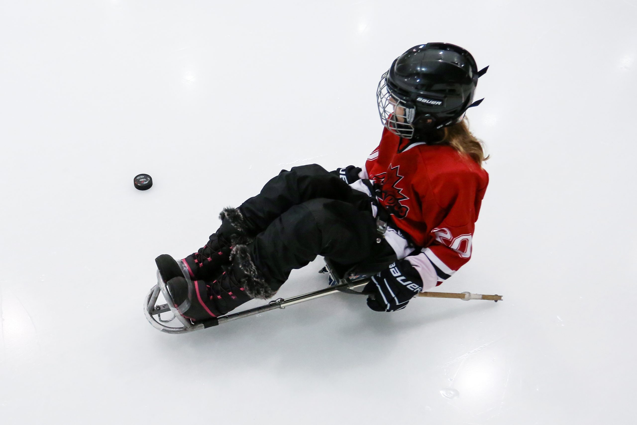 Description de l'image : Plan de haut sur un enfant assis dans une luge de parahockey qui regarde la rondelle