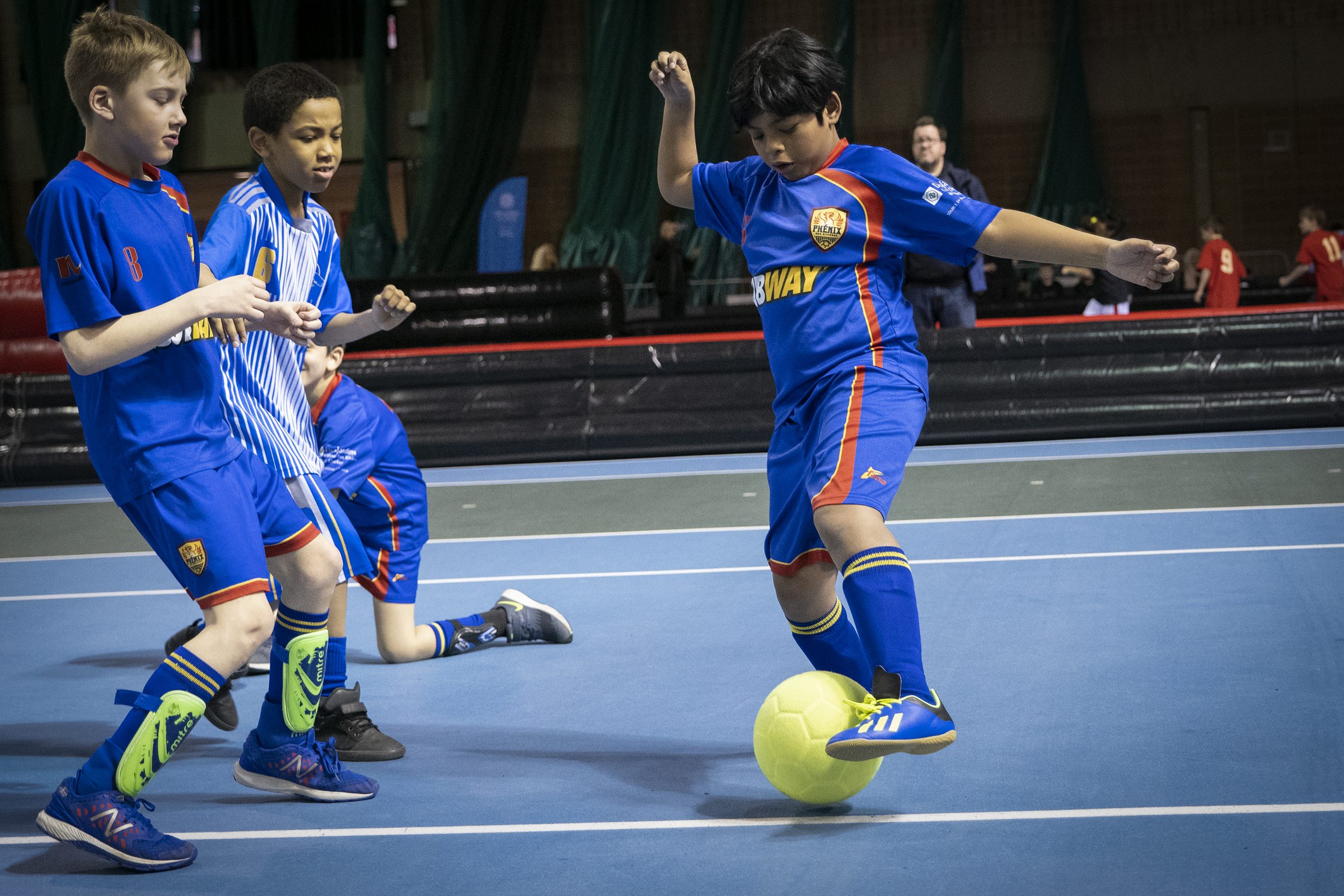Description de l'image : Au centre, un jeune joueur de soccer dibble avec le ballon devant un coéquipier et un adversaire.