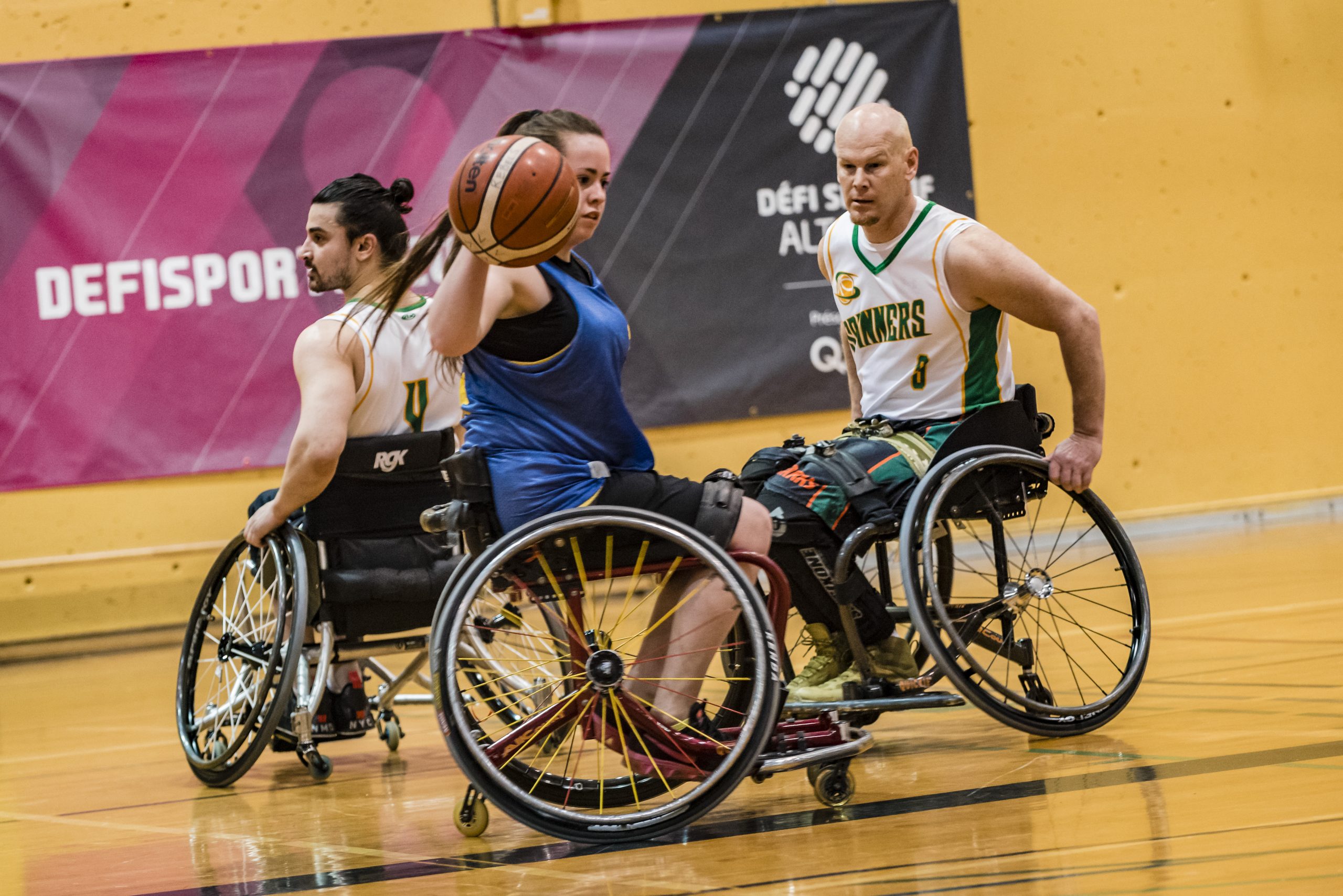 Description de l'image : Au centre, une athlète de basketball en fauteuil dribble avec le ballon. Un adversaire près d'elle la regarde.