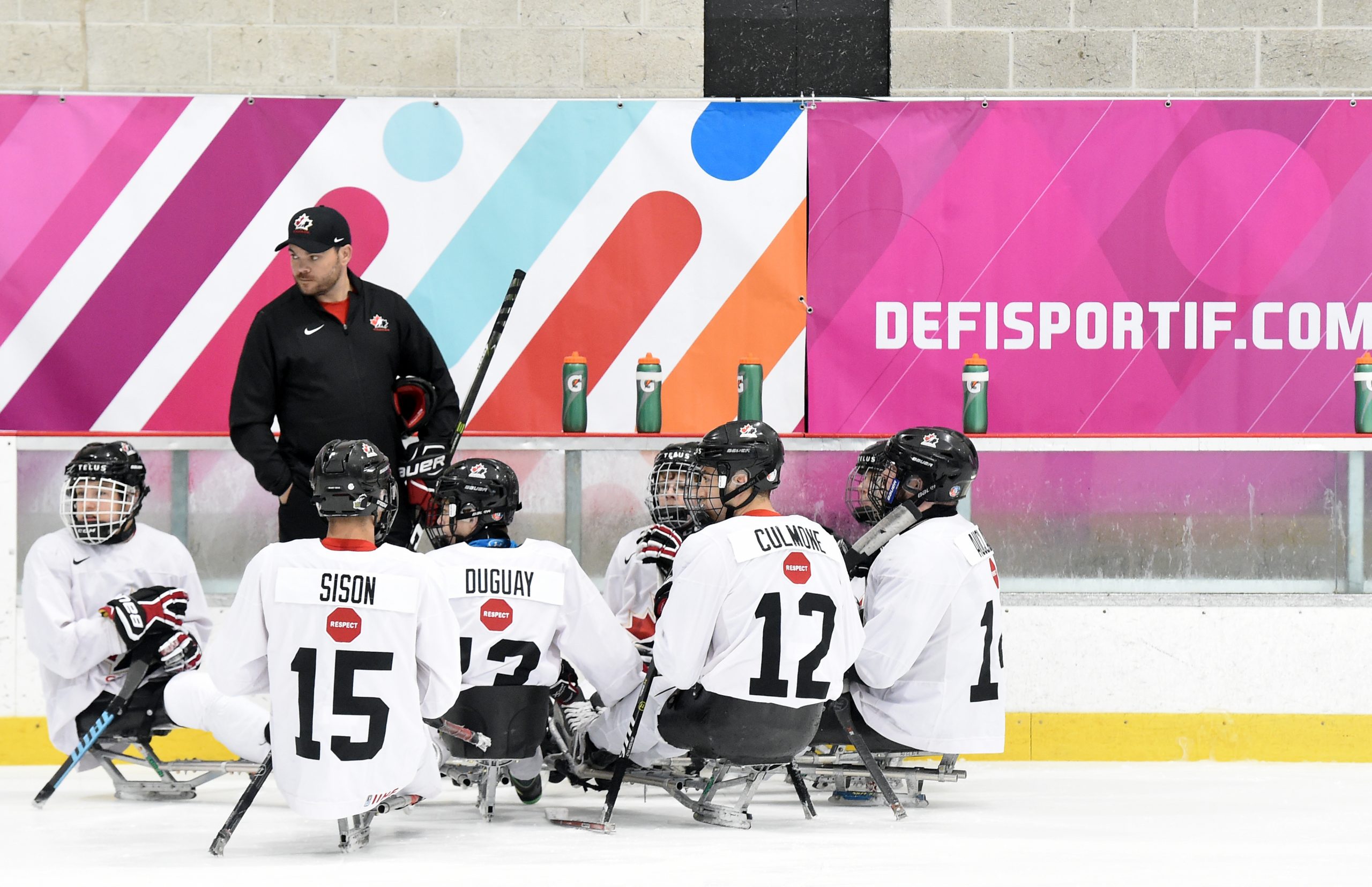 Description de l'image : L'équipe nationale canadienne de développement en parahockey se consulte sur la glace en compagnie de l'entraîneur.