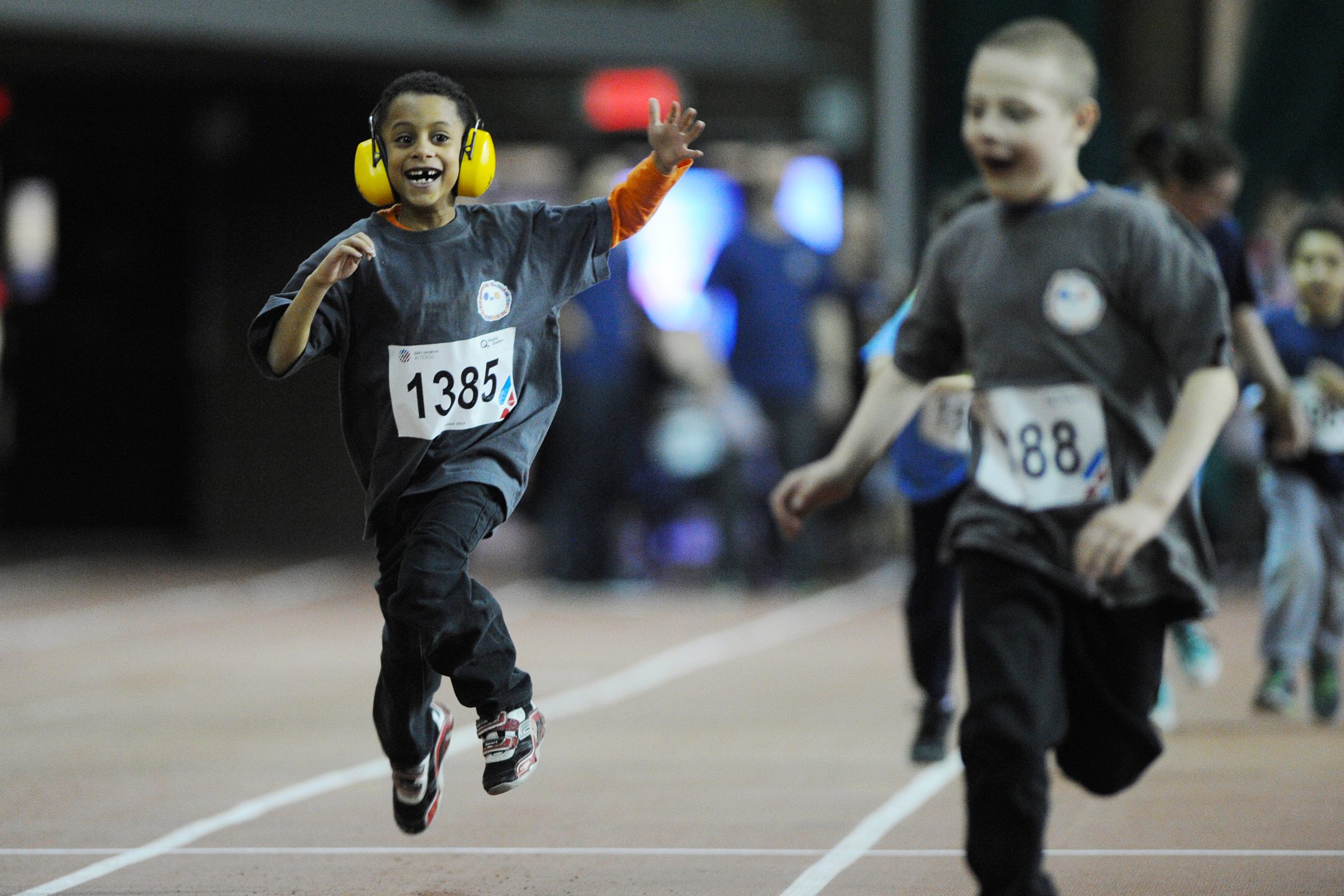 Description de l'image : Au centre, un jeune garçon portant un casque antibruit court lors d'une épreuve d'athlétisme.