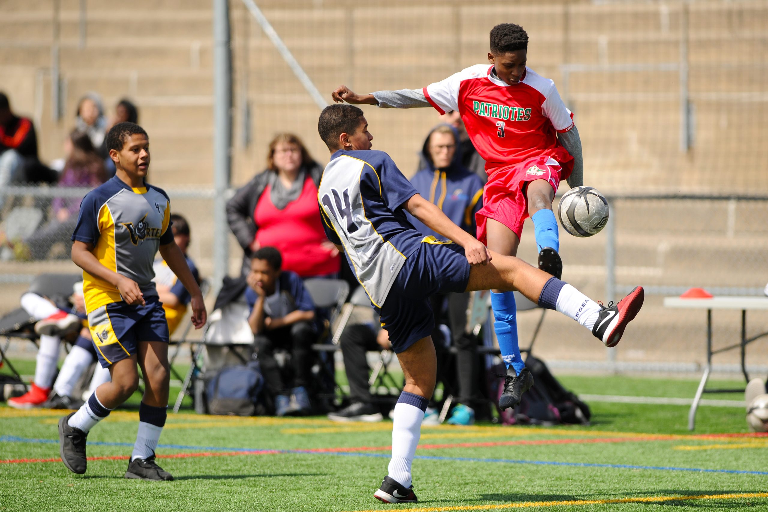 Description de l'image : Au centre, deux jeunes joueurs de soccer se disputent le ballon. L'un des deux joueurs est dans les airs.
