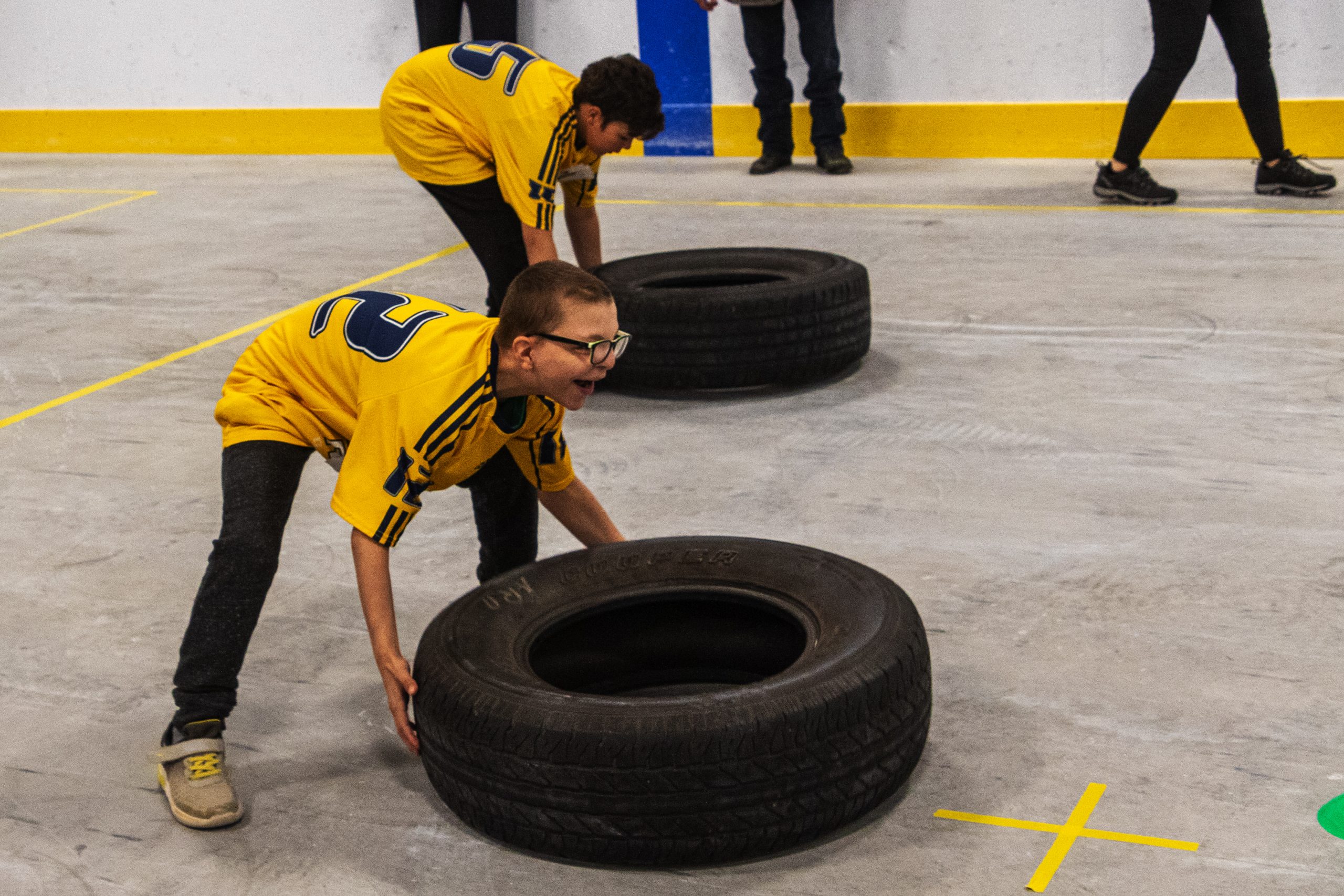 Deux garçons sont penché pour soulever chacun leur pneu lors d'une épreuve du circuit fonctionnel
