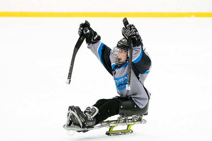 Un jeune joueur de parahockey célèbre avec les deux bras dans les airs.