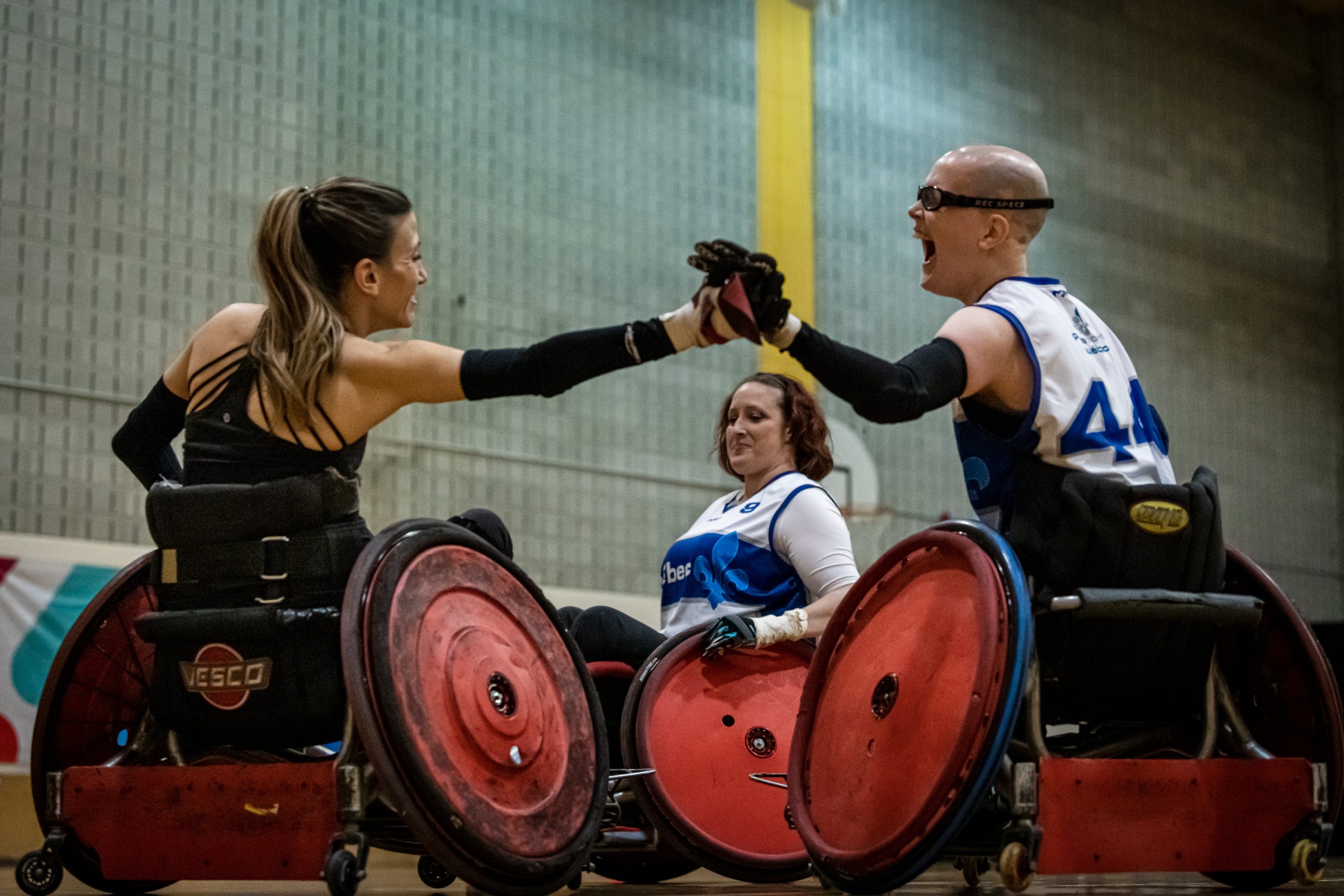 Deux joueuses de rugby en fauteuil roulant se tiennent la main de manière amicale.